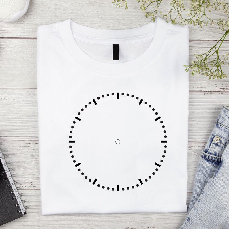 May include: White t-shirt with a black clock face design. The clock face has a circle with black tick marks around the edge.