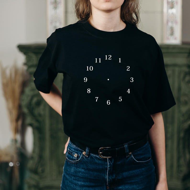 May include: A black t-shirt with a white clock face design. The numbers 1 through 12 are displayed on the clock face.