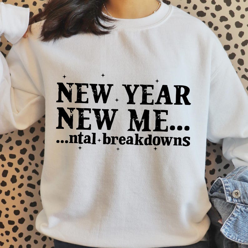 May include: White sweatshirt featuring the text "NEW YEAR NEW ME... ...ntal breakdowns" in black. The sweatshirt has a crew neck and long sleeves. The text is in a bold, sans-serif font.
