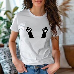 May include: White t-shirt featuring a playful design of two black cat paws with white paw pads. The paws are positioned to appear as if they are reaching up. The shirt is made of a soft, comfortable material.