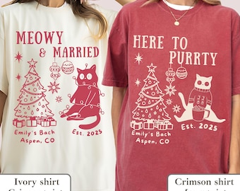 May include: Ivory and crimson t-shirts with holiday-themed cat graphics. One shirt says "Meowy & Married" with a cat wrapped in lights, a Christmas tree, and "Est. 2025." The other says "Here to Purrty" with a cat holding a mug.