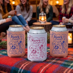 以下が含まれることがあります： 「Happy Camper」の文字とグラフィックデザインが施された、3つの缶クーラー。ピンクと白を基調とし、青とピンクのイラストが描かれています。「Olivia's Bachelorette Lake Tahoe, Ca」の文字も印刷されています。