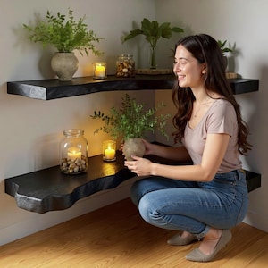 Puede incluir: Estanter&iacute;as de esquina de madera negra con un dise&ntilde;o de borde vivo. Las estanter&iacute;as est&aacute;n decoradas con plantas en macetas, velas y un tarro de cristal lleno de piedras. Una persona sostiene una planta en maceta.