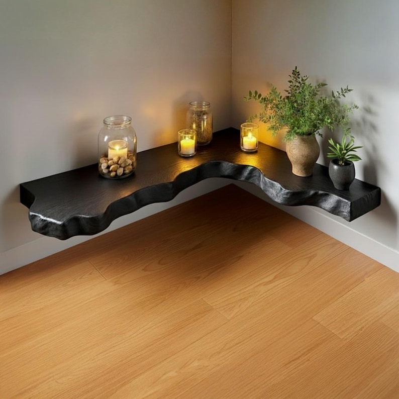 Puede incluir: Una estanter&iacute;a esquinera negra con borde vivo y borde natural ondulado. La estanter&iacute;a contiene un tarro de cristal con piedras y una vela, dos velas peque&ntilde;as y un jarr&oacute;n con vegetaci&oacute;n. La estanter&iacute;a est&aacute; montada en una pared blanca sobre un suelo de madera.
