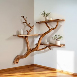 Op de afbeelding: Een unieke, handgemaakte houten hoekplankeenheid ontworpen om op een boom te lijken. De eenheid heeft drie planken die worden ondersteund door natuurlijke takken, met decoratieve items zoals planten en vazen. Het hout heeft een warme, natuurlijke afwerking.