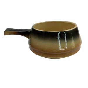 May include: A ceramic soup bowl with a handle, featuring a gradient of colors from dark brown to tan. The bowl has a rounded shape with a slightly flared rim and a single handle. The exterior has a glossy finish.