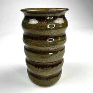 May include: A handcrafted, olive green ceramic vase with a glossy finish. The vase features a unique, ridged design, with a series of rounded bands stacked on top of each other. The vase has a slightly flared rim and a sturdy base. This decorative vase is perfect for displaying flowers.
