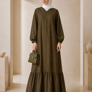 May include: An olive green long-sleeved maxi dress with a V-neckline, gathered cuffs, and a ruffled hemline. The dress is paired with a matching olive green structured handbag featuring a top handle and a gold-toned clasp closure.