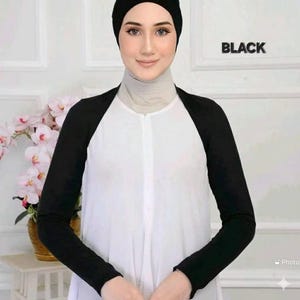 May include: A black sleeve cover with a white shirt. The sleeves are long and cover the arms. The shirt has a white body with a high neckline. The word "BLACK" is printed in the upper right corner.