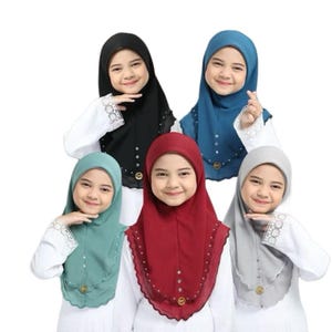 May include: Five young girls wearing colorful hijabs. The hijabs are in black, blue, teal, red, and gray. Each hijab has a decorative trim and embellishments. The girls are wearing white shirts with lace trim.