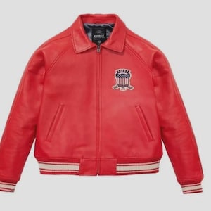 May include: A red leather jacket with a zip-up front, a collar, and a patch on the chest. The jacket has white and red striped cuffs and waistband. The patch features the word "AVIREX".