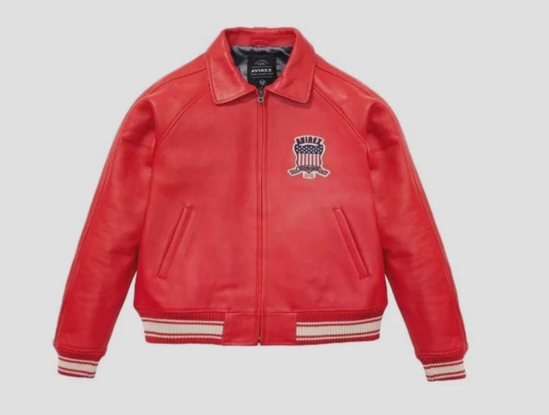 May include: A red leather jacket with a zip-up front, a collar, and a patch on the chest. The jacket has white and red striped cuffs and waistband. The patch features the word "AVIREX".