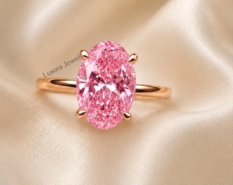 May include: A ring featuring a large, oval-cut pink gemstone set in a polished rose gold band with four prongs. The text Luxora Jewels is visible on the left side of the stone. The ring has a smooth, thin metal band and a faceted pink center stone.