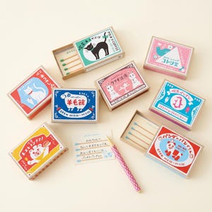May include: A selection of illustrated matchboxes, featuring designs such as a black cat, a sheep, a rabbit, a penguin, and a panda. The boxes are in various colours and include Japanese text.