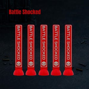 May include: Five red markers with the text "Battle Shocked" in white. Each marker has a white skull icon. The markers are standing upright on a dark surface.