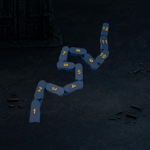 May include: A dark blue, segmented object with the numbers 1 through 12 in gold, arranged in a winding pattern. The object is on a dark, textured surface, with small, scattered metallic pieces.
