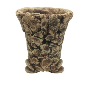 Puede incluir: Un pequeño macetero de cerámica marrón con una superficie rugosa y texturizada. El macetero tiene una abertura ancha y redonda y una base estrecha con tres pequeños pies.