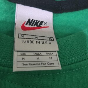 May include: Close-up of a green and black shirt with a Nike label. The label includes the Nike logo, size information, and "MADE IN U.S.A." The shirt is a medium size.