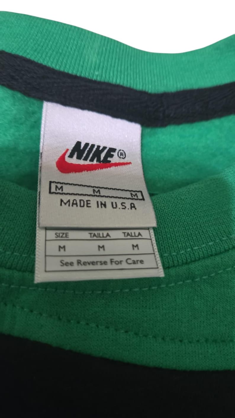 May include: Close-up of a green and black shirt with a Nike label. The label includes the Nike logo, size information, and "MADE IN U.S.A." The shirt is a medium size.