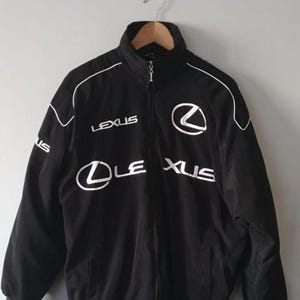 Peut inclure: Une veste noire zippée arborant le logo et le texte Lexus brodés en blanc sur la poitrine et les manches. La veste présente un col montant, des manches longues avec des détails passepoilés blancs et une fermeture éclair frontale intégrale.