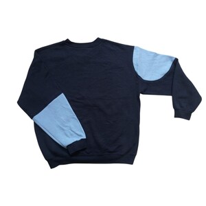 K&ouml;nnte beinhalten: Ein marineblaues Sweatshirt mit hellblauen Farbblock-Akzenten an den &Auml;rmeln. Das Sweatshirt hat einen Rundhalsausschnitt und lange &Auml;rmel. Die hellblauen Bereiche befinden sich am Oberarm und am unteren &Auml;rmel.
