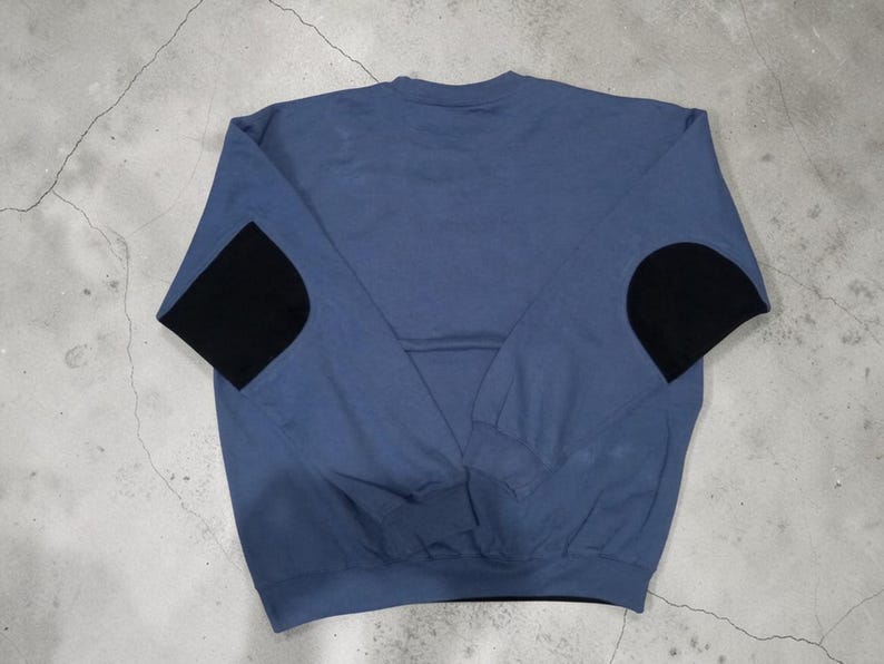 May include: A blue sweatshirt with black elbow patches. The long-sleeved top is a solid blue color with a crew neck and black patches on the elbows. The garment is made of a soft material.