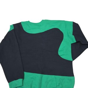 May include: A green and black crew neck sweatshirt. The garment has a distinctive design, with a large black shape across the chest and upper back, contrasted by green sleeves and a green lower section.