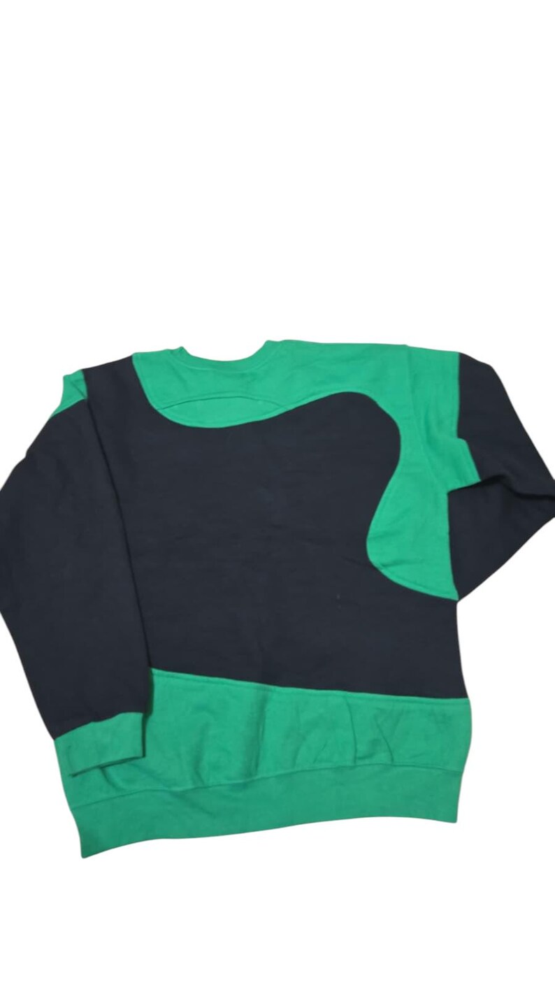 May include: A green and black crew neck sweatshirt. The garment has a distinctive design, with a large black shape across the chest and upper back, contrasted by green sleeves and a green lower section.