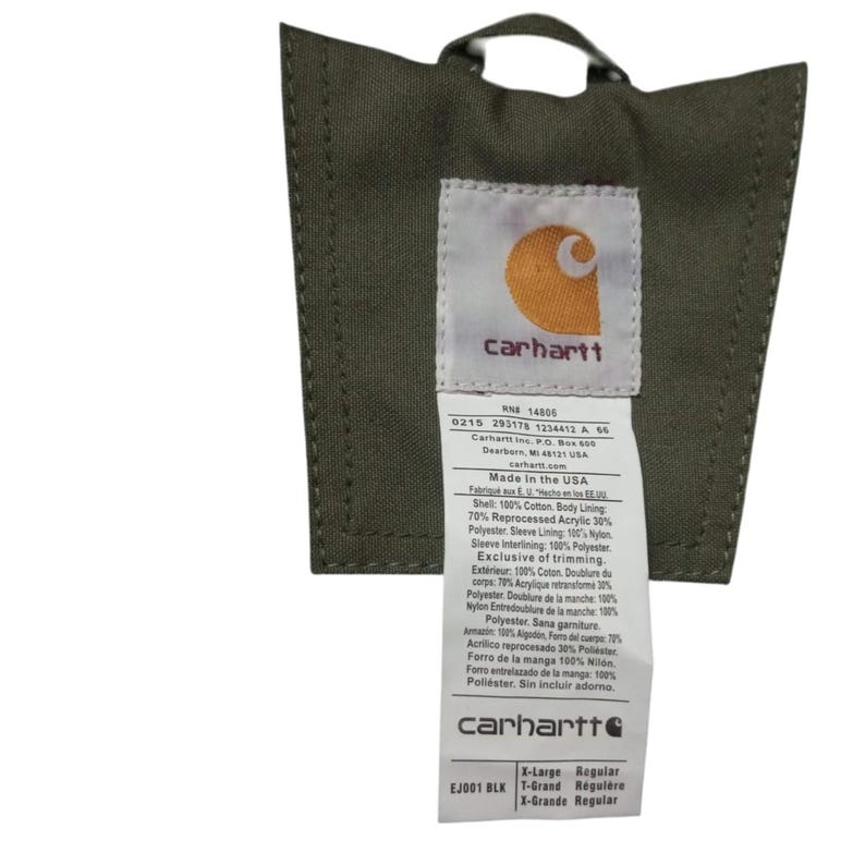 May include: Close-up of a Carhartt jacket tag. The tag is olive green with a white label featuring the Carhartt logo and product information. The tag includes details about the jacket's materials, such as cotton, acrylic, and polyester.