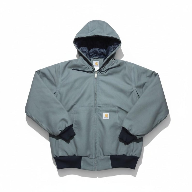 May include: A hooded, zip-up work jacket in a muted teal color. The jacket features a dark navy blue lining in the hood and cuffs, and a small logo patch on the chest. The jacket has two front pockets and a ribbed hem.