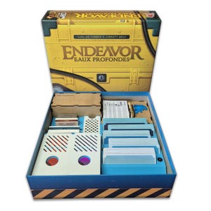 Op de afbeelding: Open gele bordspeldoos met de titel "Endeavor Eaux Profondes" in gouden letters. De blauwe binnenkant bevat kaarten, fiches en een houten organizer. De onderkant van de doos heeft een zwart en geel gestreept ontwerp. Spel van Carl de Visser & Jarratt Gray.