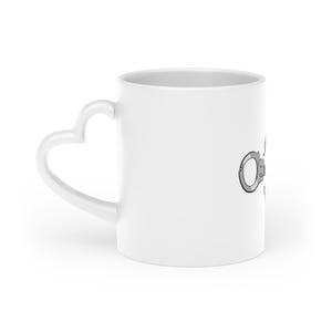May include: White ceramic mug with a heart-shaped handle. The mug features a grey illustration of handcuffs. The mug is designed for beverages and has a simple, clean aesthetic.