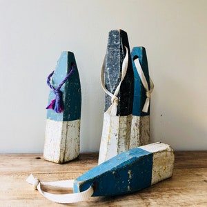 May include: Four wooden nautical buoys with white and blue paint. The buoys have white rope loops attached to them. The buoys are sitting on a wooden surface.