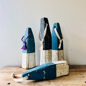May include: Four wooden nautical buoy floats with white and blue paint. The buoys have rope loops and are weathered and distressed.