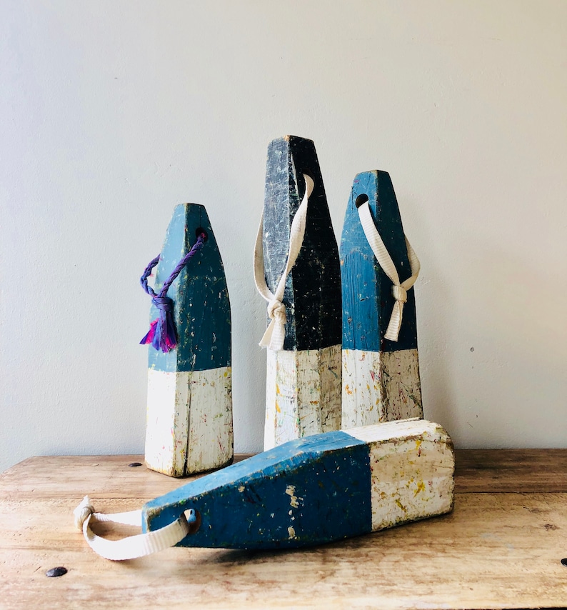 May include: Four wooden nautical buoy floats with white and blue paint. The buoys have rope loops and are weathered and distressed.