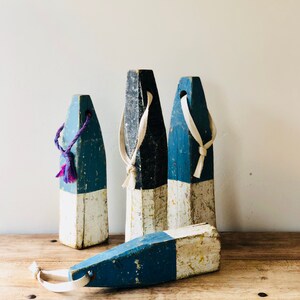May include: Four wooden nautical buoys painted in blue and white with white rope handles. The buoys are weathered and have a rustic look.