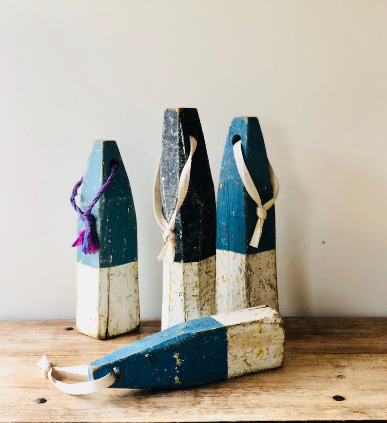 May include: Four wooden nautical buoys painted in blue and white with white rope handles. The buoys are weathered and have a rustic look.