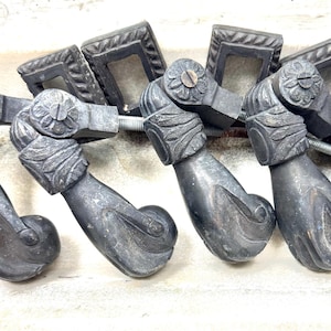 Peut inclure: Ensemble de poignées de tiroir antiques en métal gris foncé. Chaque poignée présente un motif floral décoratif sur la poignée et une plaque arrière carrée. Les poignées sont reliées par une tige métallique.