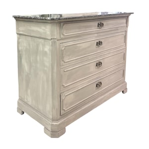 May include: A four-drawer chest of drawers with a gray marble top. The chest is painted in a distressed light gray finish. Each drawer has a decorative silver-toned handle. The chest sits on four short, square feet.