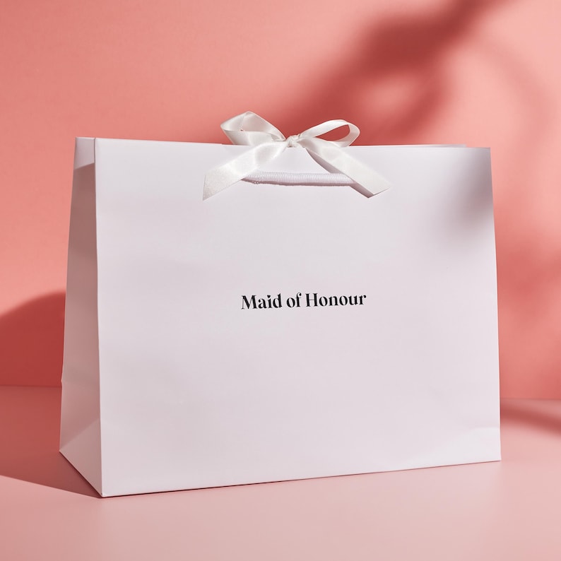 May include: White gift bag with a white satin ribbon bow and the text "Maid of Honour" printed in black.