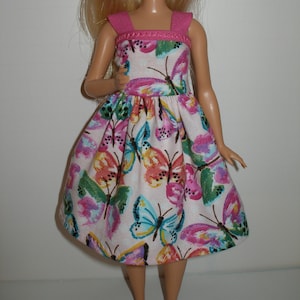May include: A white dress with a pink bodice and a butterfly print. The dress has a gathered skirt and thin straps.