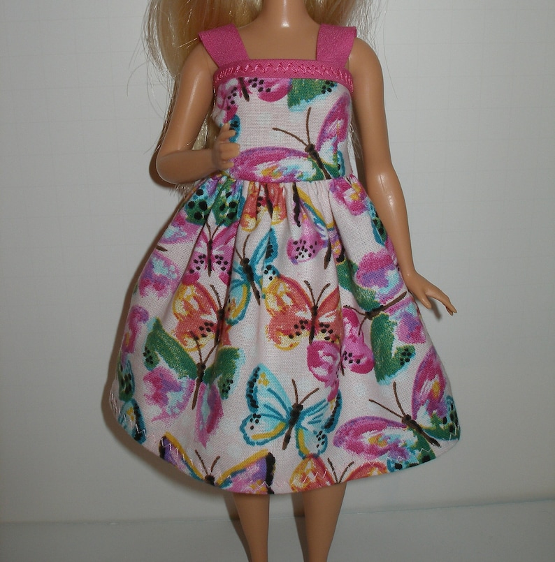 May include: A white dress with a pink bodice and a butterfly print. The dress has a gathered skirt and thin straps.