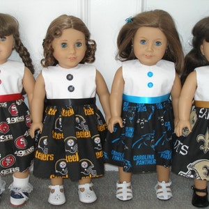 May include: Four dolls wearing dresses with white tops and black skirts. The skirts feature NFL team logos and names, including the 49ers, Steelers, Panthers, and Saints. Each dress has a ribbon at the waist and button details.