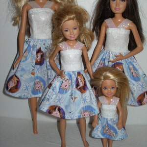 Puede incluir: Tres mu&ntilde;ecas con vestidos blancos con purpurina y faldas azules con un estampado de Frozen. Las mu&ntilde;ecas est&aacute;n de pie sobre una superficie blanca.