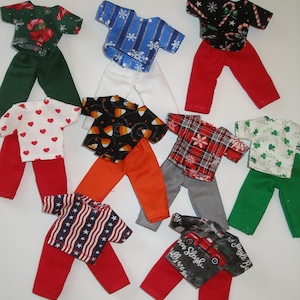 May include: A collection of doll-sized outfits, each featuring a patterned top and matching pants. Designs include hearts, snowflakes, candy corn, and patriotic stars and stripes. Colors include red, green, white, and blue.
