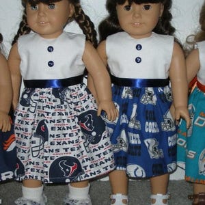 May include: Two dolls wearing white sleeveless tops with navy blue buttons and a navy blue ribbon belt. One doll has a skirt with a Houston Texans football theme, and the other has a skirt with a Colts theme. Both dolls wear white shoes.