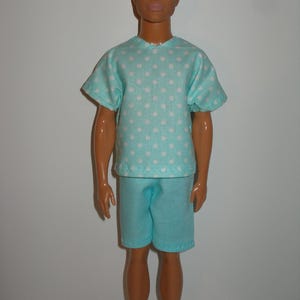 K&ouml;nnte beinhalten: Eine Puppe in einem hellblauen Pyjama-Set. Das kurz&auml;rmelige Oberteil ist mit wei&szlig;en Punkten gemustert. Die passenden Shorts vervollst&auml;ndigen das Outfit. Die Puppe hat blondes Haar und blaue Augen.