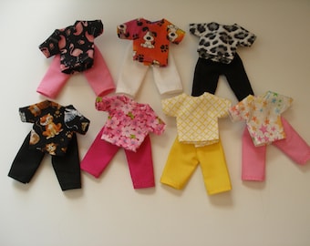 May include: Seven sets of doll clothing, each consisting of a short-sleeved t-shirt and pants. The outfits feature various patterns including flamingos, dogs, leopard print, cats, flowers, yellow grid, and colorful stars, paired with pink, white, black, and yellow trousers.