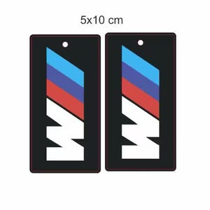 Könnte beinhalten: Zwei schwarze Auto-Lufterfrischer-Aufkleber mit einem weißen BMW-Logo und blauen, roten und weißen Streifen. Die Aufkleber sind 5x10 cm groß.