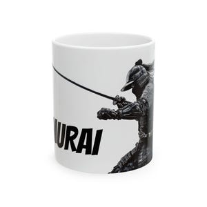 Puede incluir: Taza de cerámica blanca con una ilustración en blanco y negro de un guerrero samurai sosteniendo una espada. La palabra "Samurai" está impresa en negro en la parte inferior de la taza.